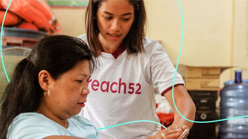 Two women from Reach52 look at a mobile device.