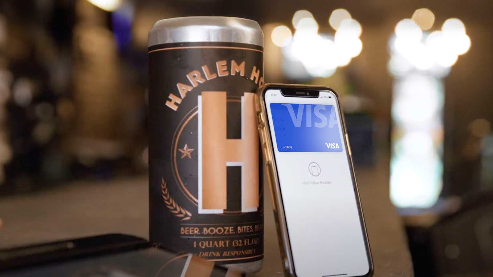 Smartphone showing a Visa-branded card leaning against a can of Harlem Hops.