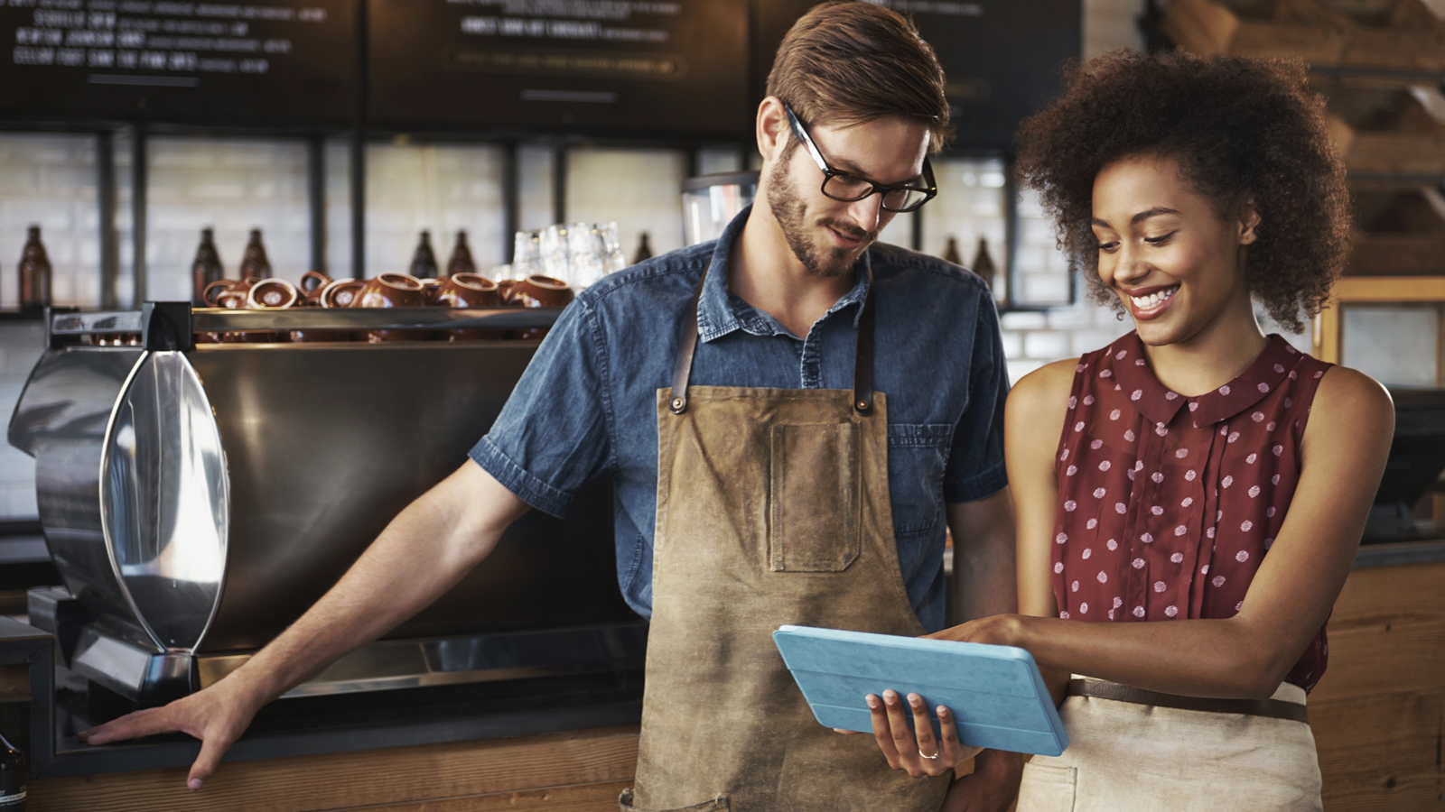 A smiling woman and man standing inside a coffee shop looking at a digital tablet. A smiling woman and man standing inside a coffee shop looking at a digital tablet.