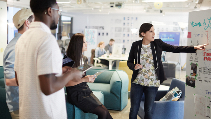 Three people looking at a woman pointing at a diagram on a whiteboard. Three people looking at a woman pointing at a diagram on a whiteboard.