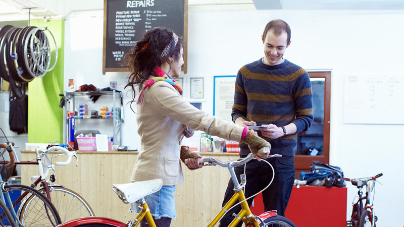 A woman standing happily with her her bicycle in a local bike shop. A woman standing happily with her her bicycle in a local bike shop.