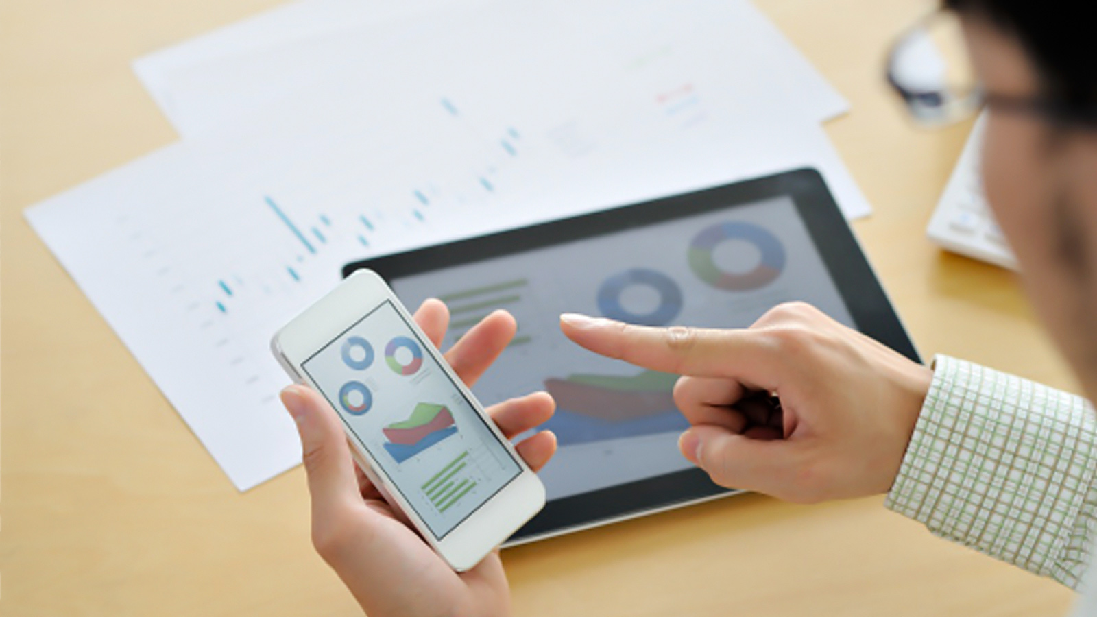 Man working on smartphone showing a business graphic with a tablet on the desk in the background. Man working on smartphone showing a business graphic with a tablet on the desk in the background.