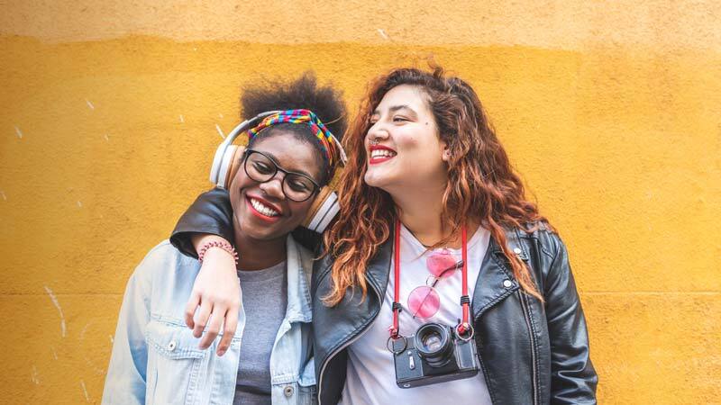 two women with arms around each other in front of yellow wall