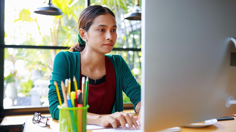 Woman sitting at desk looking at computer screen.