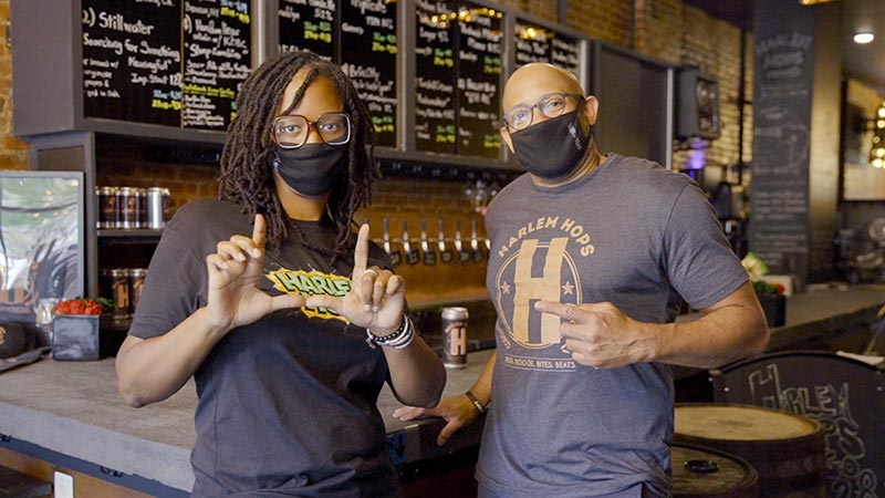 A woman and a man in COVID masks pose in front of a bar.