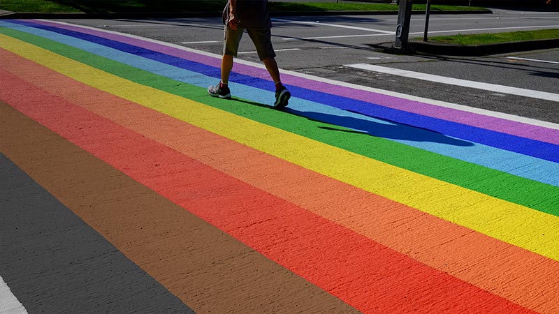 Person walking across a pride-inspired rainbow flag crosswalk.