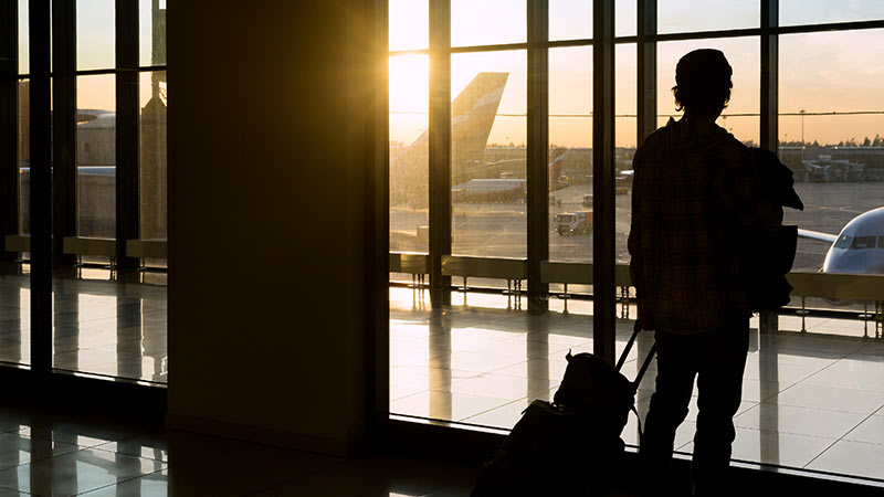 silhouette of passenger looking out airport window onto tarmac