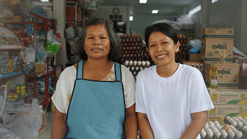 Two woman smiling, looking at the camera standing inside a grocery store.