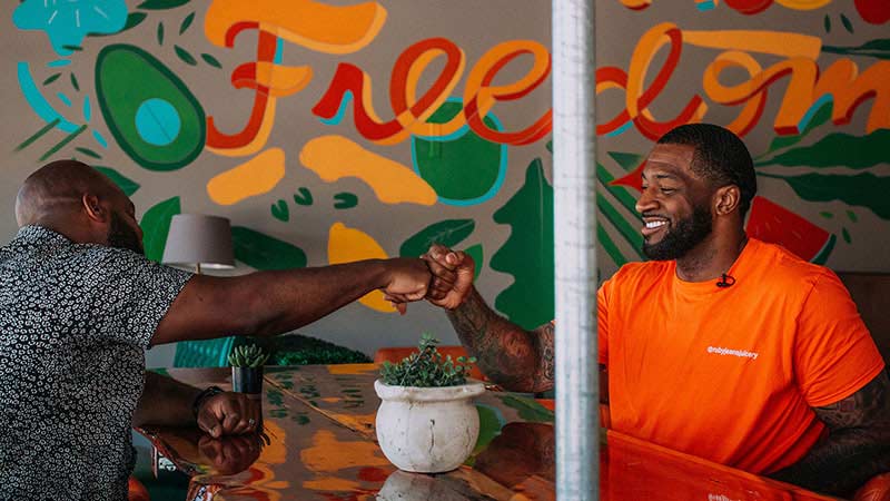 Two men sit at a table in front of a mural that says freedom