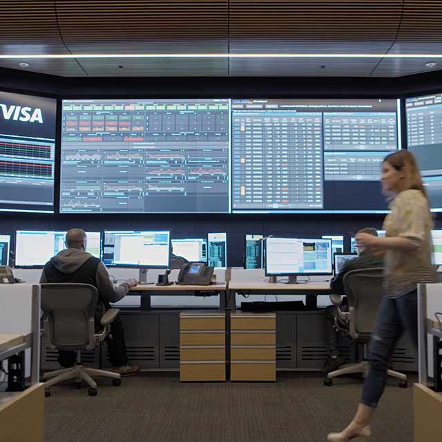 A man working in a security intelligence office and a woman walking by.