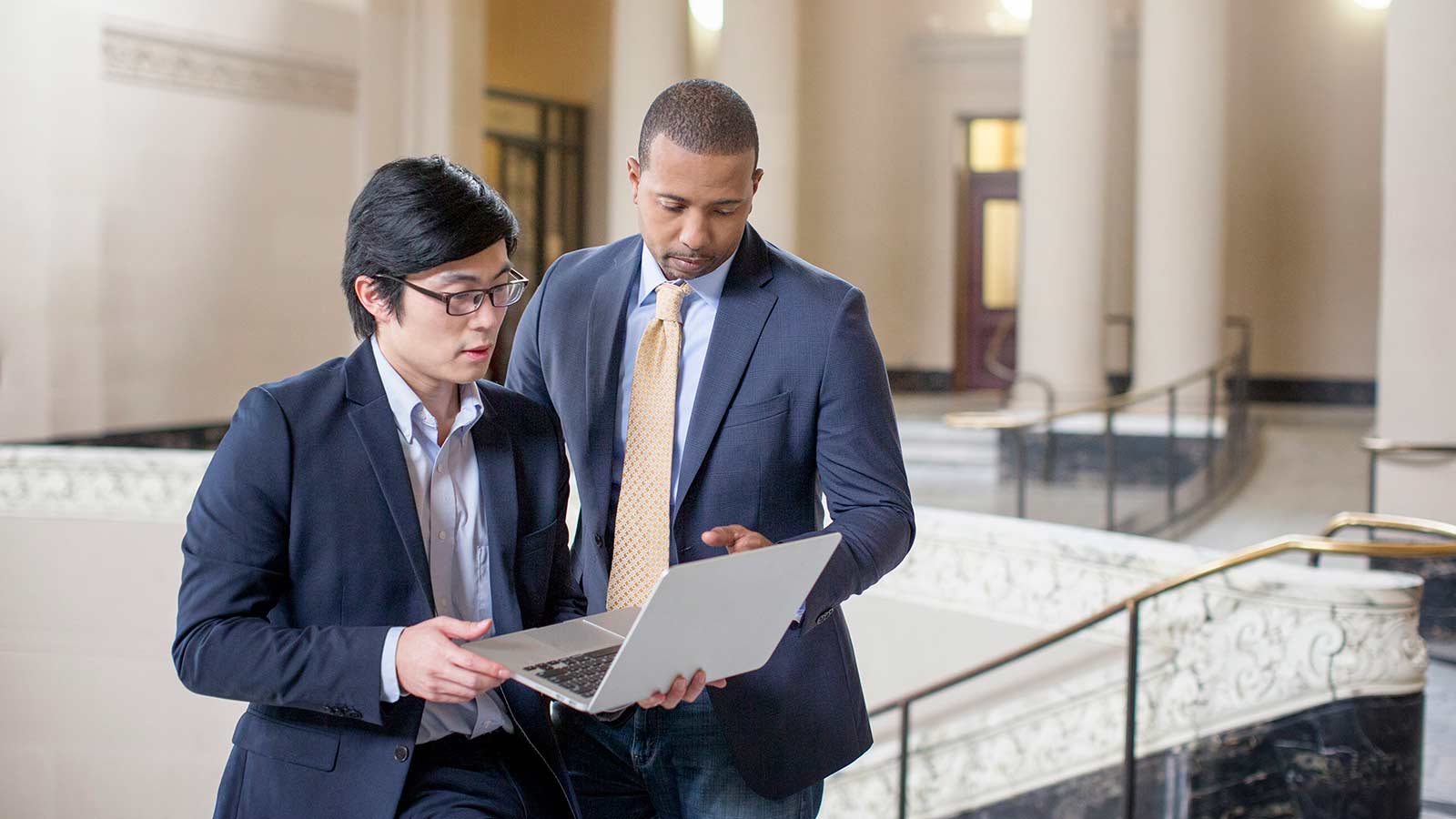 Two business men standing and conversing while looking at a laptop. Two business men standing and conversing while looking at a laptop.
