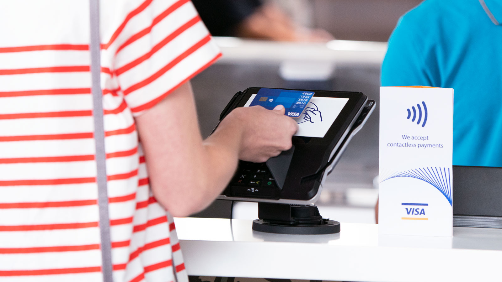 Woman paying with a Visa contactless card at a counter.