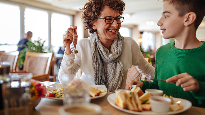941145654 A woman and boy smiling and enjoying their food at a restaurant.
