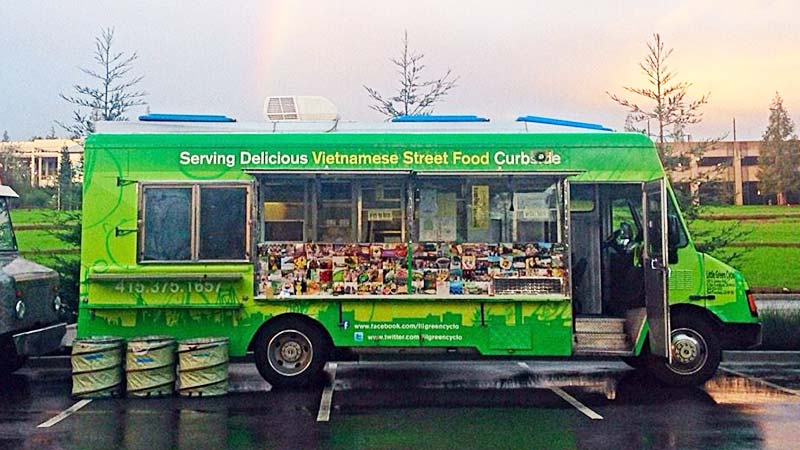 Profile of the Little Green Cyclo food truck with their slogan 'Serving Delicious Vietnamese Street Food Curbside' front and center parked in a parking lot open for business.