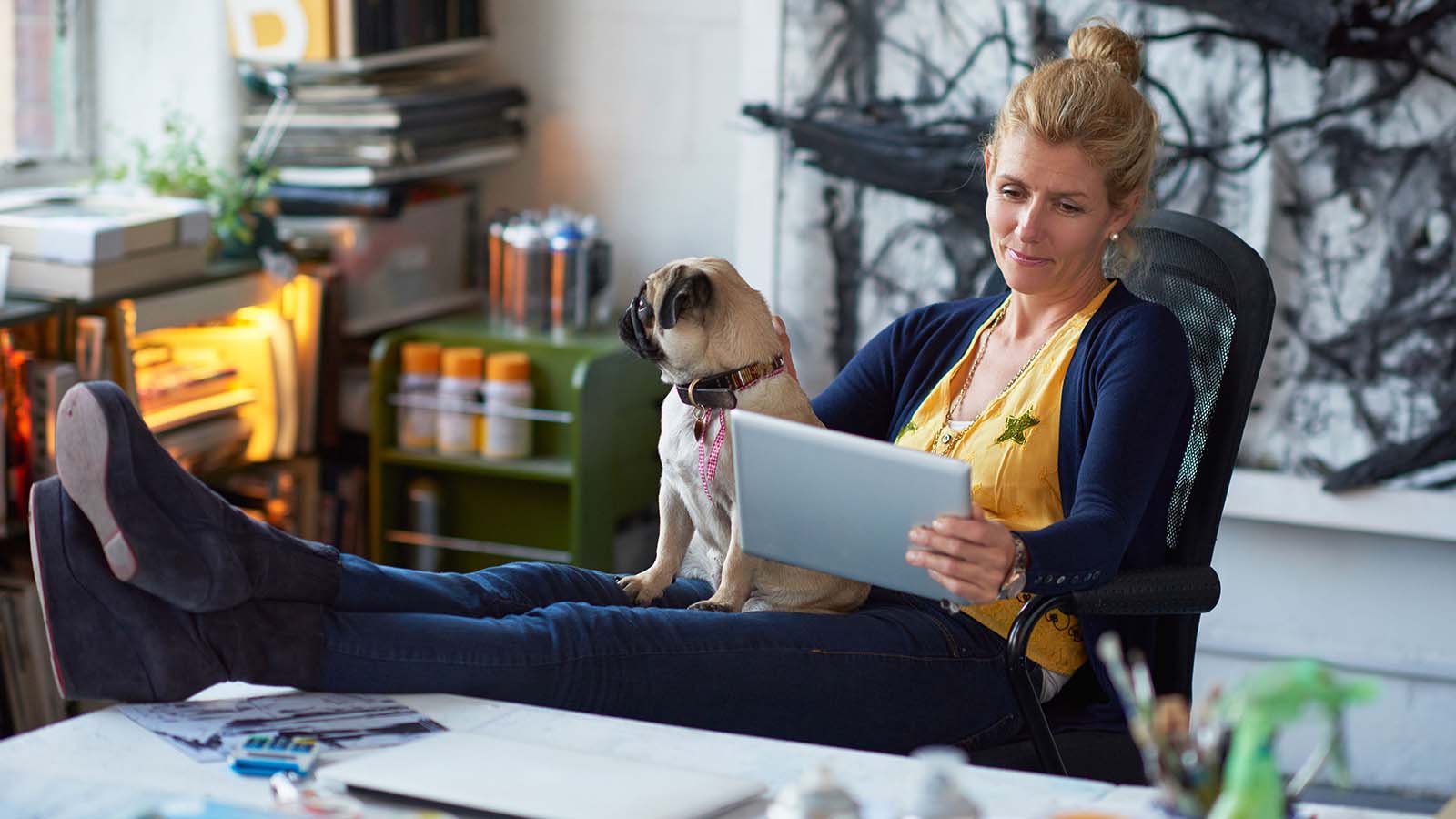 Woman with her feet on a desk and a dog in her lap reading a tablet. Woman with her feet on a desk and a dog in her lap reading a tablet.