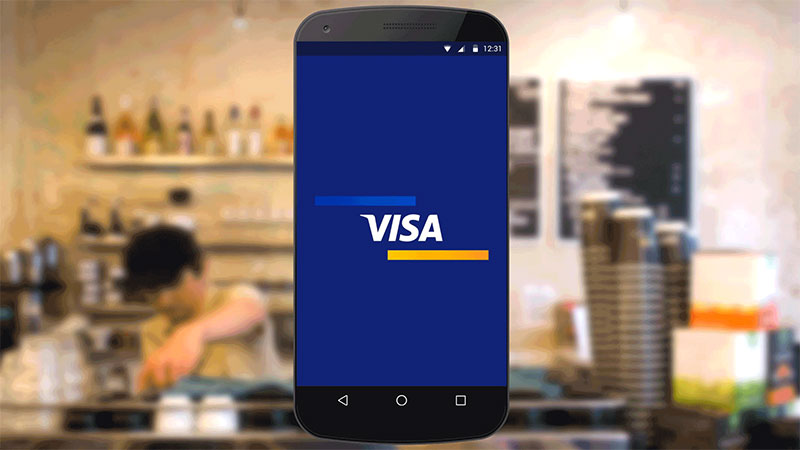 Visa logo displayed on smart phone superimposed over background of a coffee bar counter.