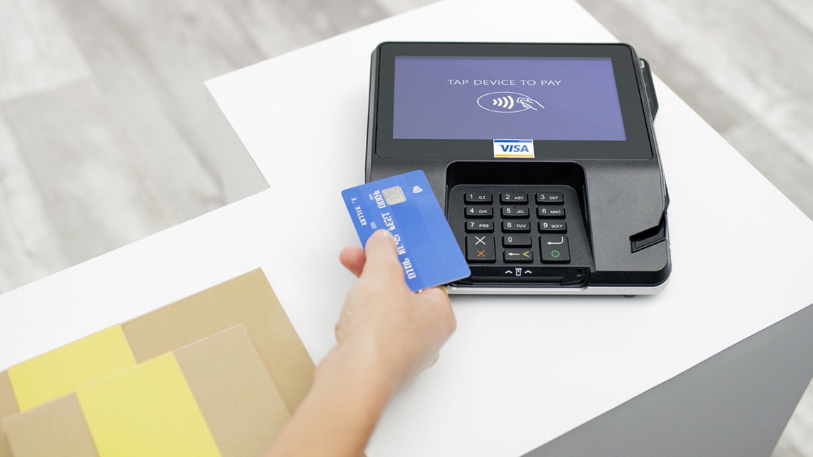 Hand holding a Visa credit card at a POS machine.