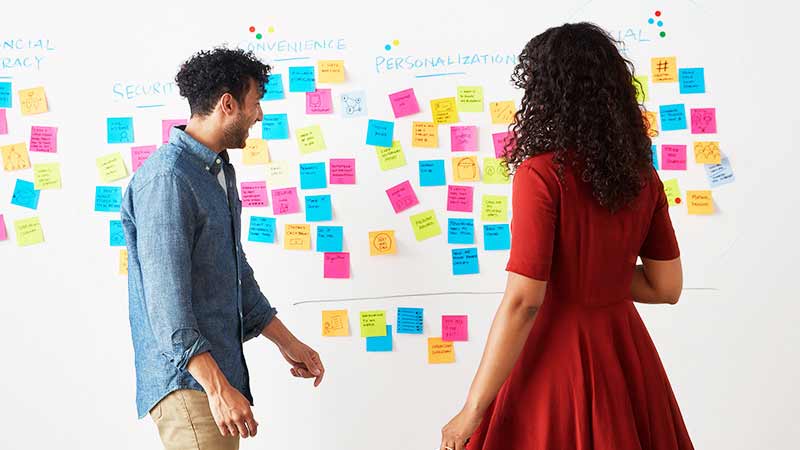 office-board-800x450 A pair of Visa employees review a white board full of sticky notes.