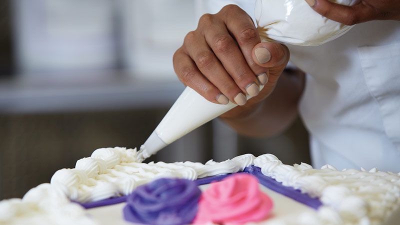 Closeup of a woman piping icing onto a Costco cake.