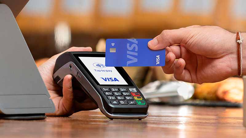 Hand tapping to pay with Visa-branded card on a Visa-branded payment terminal.