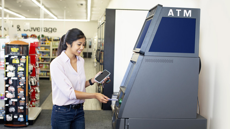 Woman using card for ATM transaction in front of a store. Woman using card for ATM transaction in front of a store.