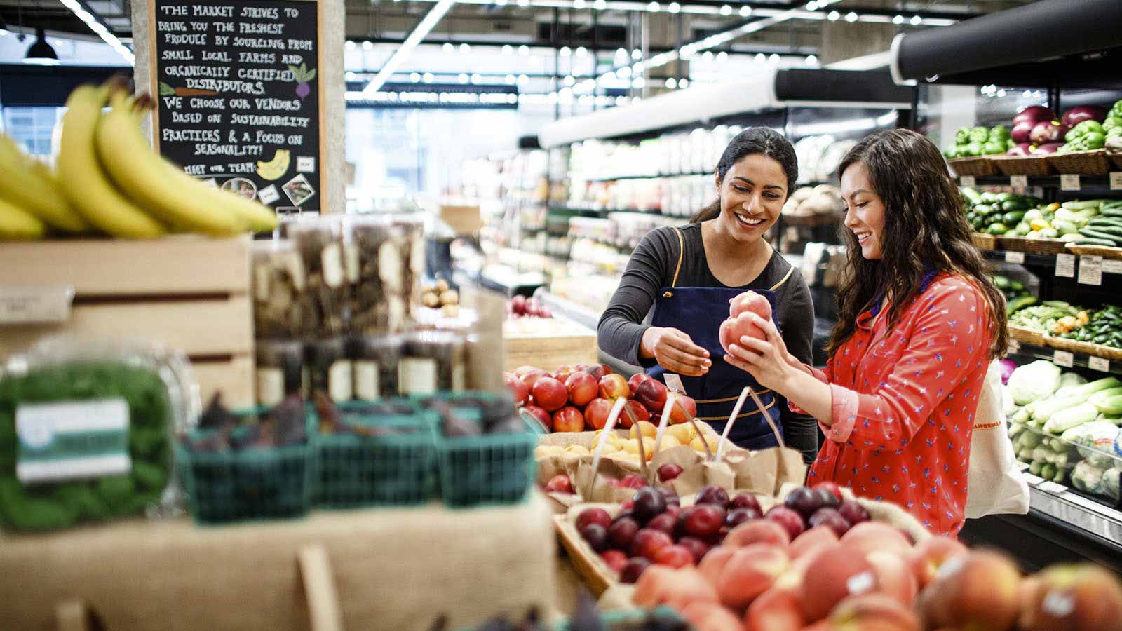 A woman shopping at a grocery store is assisted by an employee.