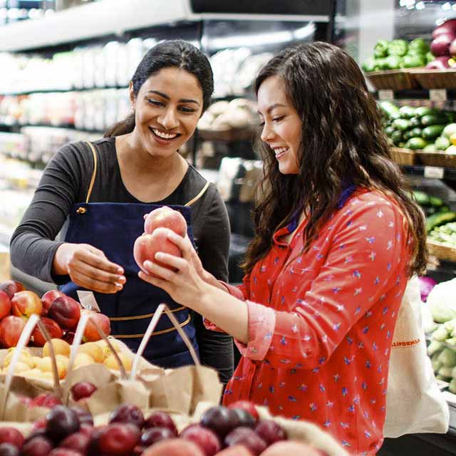 A woman shopping at a grocery store is assisted by an employee.