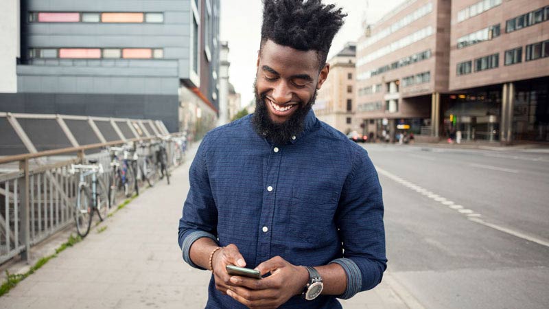 Smiling young man on the street looking at his phone.